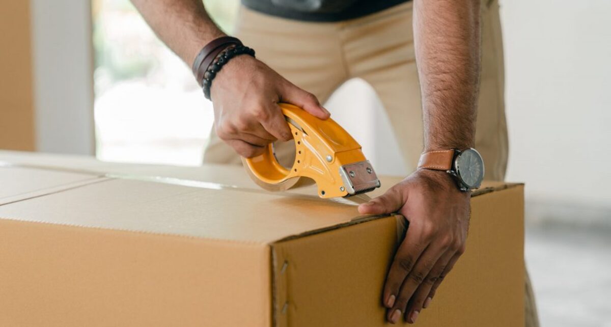 Crop man taping carrying box with scotch