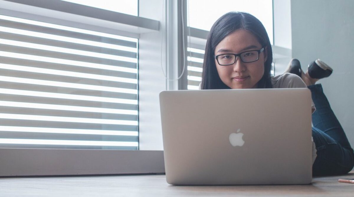 woman using silver MacBook beside clear glass window