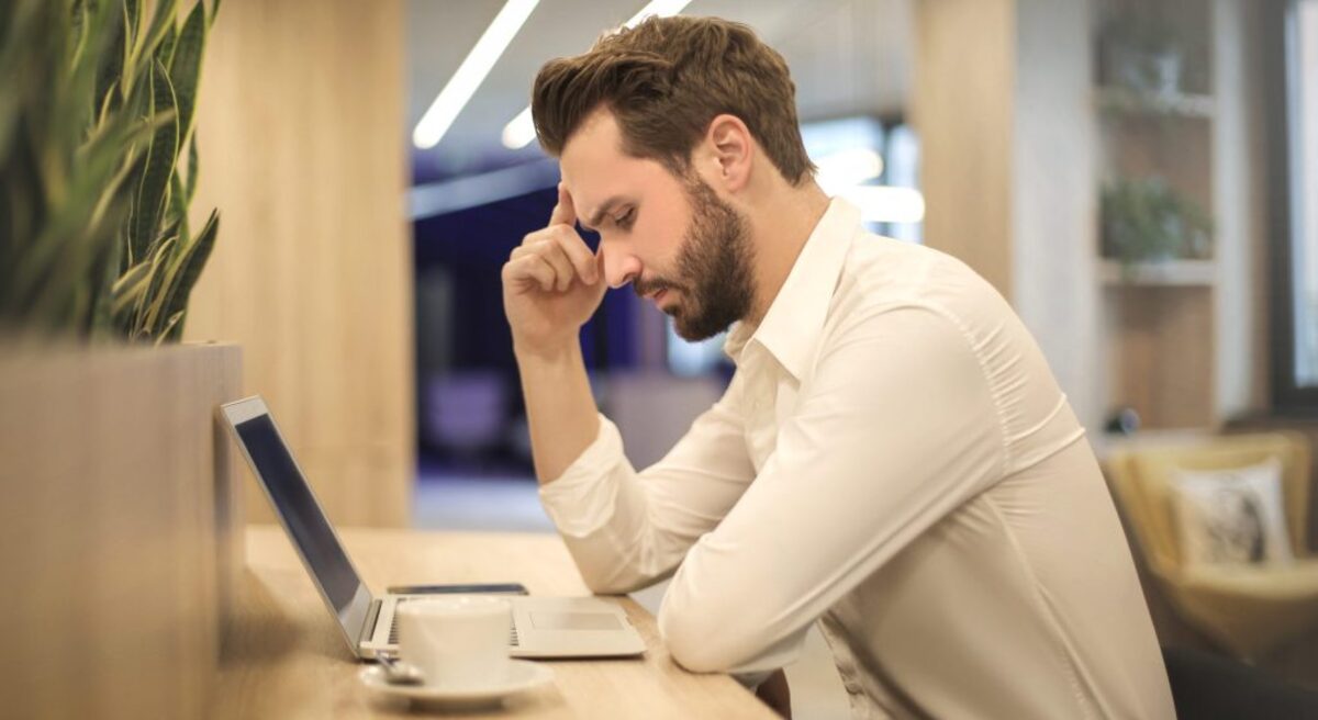 Man with hand on temple looking at laptop