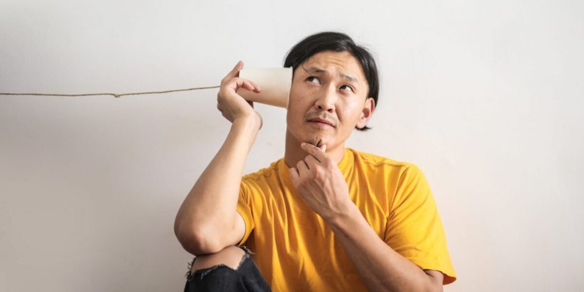 Pensive ethnic man listening to answer in paper cup phone