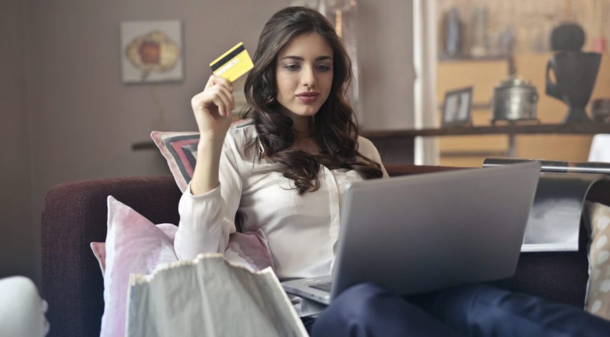 Woman holding card while operating silver laptop