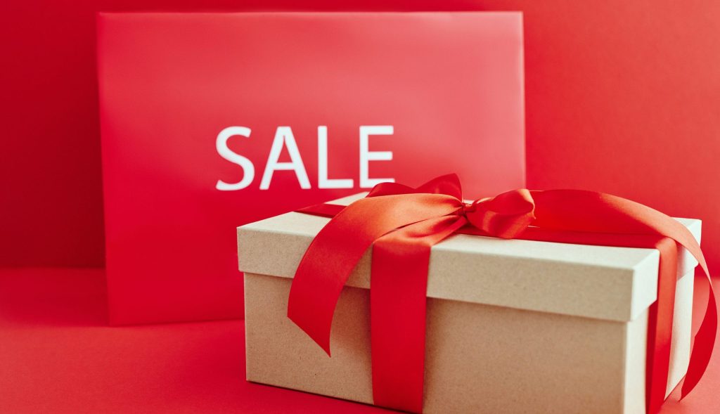 Cardboard box with red ribbon beside a sale sign