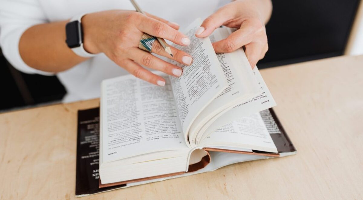 Person wearing silver ring holding white book page